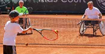 Kind spielt mit zwei Rollstuhltennisspielern